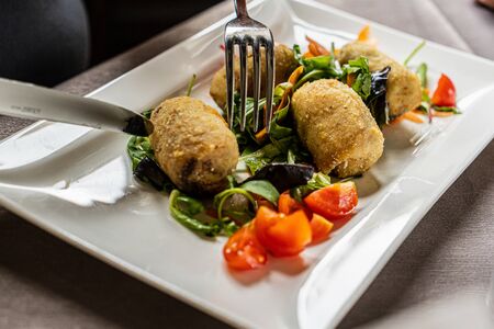Close up of an unrecognizable man or woman eating fish meat balls breaded in a square white plate. People eating healthy food conceptの写真素材