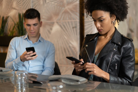 Young couple bored sitting at restaurant distracted by smartphone screen. People always connected to the internet addicted by technology concept.の写真素材