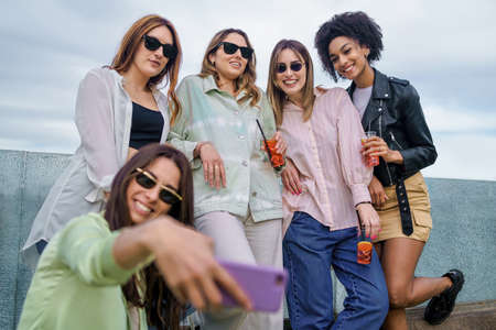 Multiracial group of female friends taking selfies on the street. They are teenagers, five girls, standing with the sky in the background. Women using tech concept.の写真素材