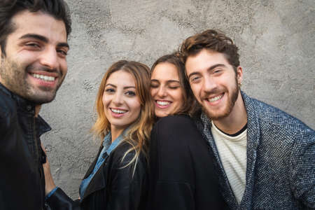 Portrait of millennials smiling at the camera. Group of young people having fun together against a concrete wall.の写真素材