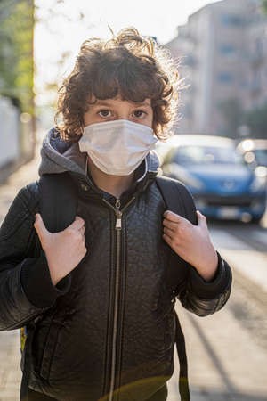 Schoolboy with backpack returning back to school with face mask. Nine year old kid walking in the street in the new normal.の写真素材