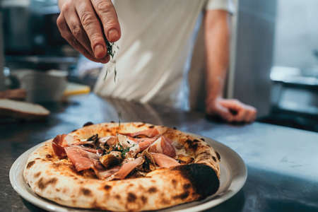 An Italian chef garnishes the pizza just out of the stone oven.の写真素材