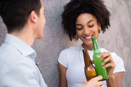 Multiracial couple of young lovers talking together holding and drinking bottles of beer. Shy African American woman with eyes closed.の写真素材