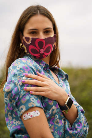 Young woman showing arm with adhesive bandage to prove vaccination against the virus. Concept of vaccinated peopleの写真素材