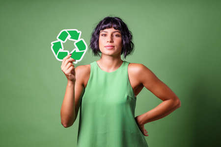 Young woman in green showing the recycle symbol isolated on a green background. Sustainability concept.の写真素材