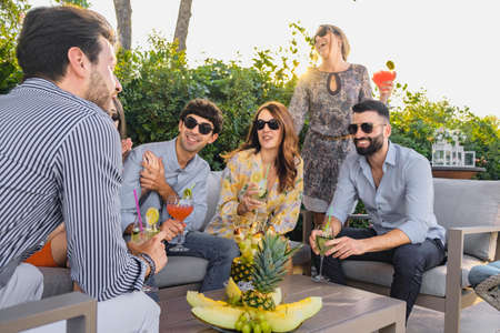 Group of happy young people gathering, talk together and have fun joking while drinking cocktails outdoors on the terraceの写真素材