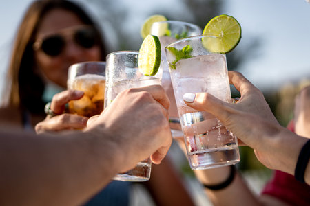 Group of young people clinking cocktail drink glasses toasting. Best friends wearing a lowered face mask having a funny reunion.の写真素材
