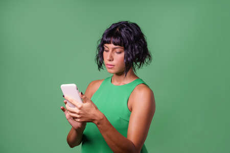 Young woman using a smartphone browsing online content against a green background. Tech concept. Studio shot.の写真素材