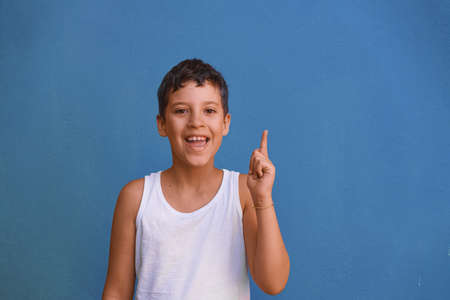 young Cute boy smiling and pointing finger upwards, isolated on blue backgroundの写真素材