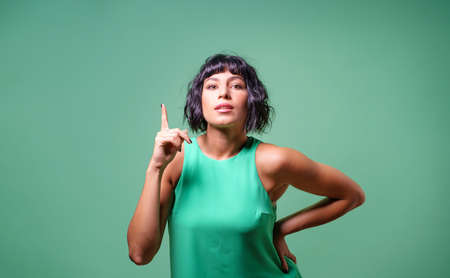 Portrait of a young woman pointing fingers up isolated on teal backgroundの写真素材