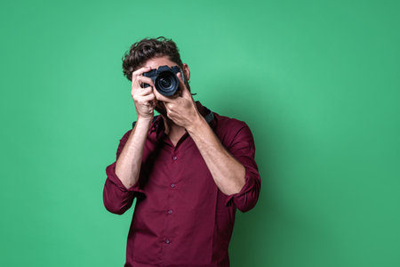Boy holding a mirrorless camera and taking a picture while looking through the electronic viewfinder.の写真素材