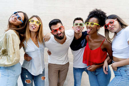 Interracial gen z young people having fun making weird faces and wearing colored glasses.の写真素材
