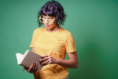 Portrait of a young student woman reading a book isolated over green background. Girl reading novel.の写真素材