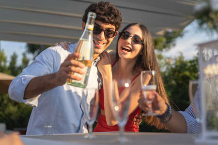 A young loving couple announces their marriage to their friends by celebrating their love with a bottle of champagneの写真素材