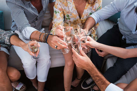 Group of young friends toasting sparkling white wine glasses at outdoor party - Friendship celebration with happy people enjoying time together at the terrace garden drinking champagneの写真素材