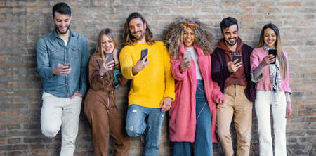 Interracial group of young people joking together using smartphones and browsing social network...