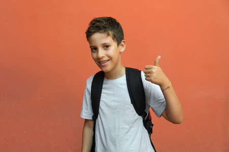 Elementary schoolboy with thumb up isolated against an orange wall. back to school concept.の写真素材