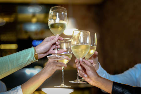 Toast at the restaurant. Detail on the clinkering white wine glasses. Concept of friends having a toast together by raising their wineglasses.の写真素材