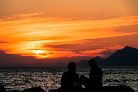 Orange sunset over the sea and in the foreground silhouettes of loversの写真素材