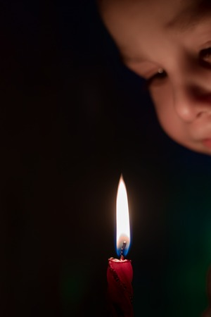 The kid looks at a burning candle flame at night. Isolate on black.の写真素材