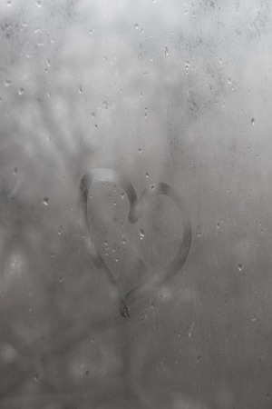 Heart of glass with rain drops on a gray sky background