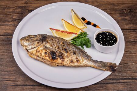Grilled fish on a white plate on the tableの写真素材