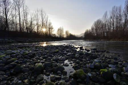 Adda river during the sun set, with the reflection of the sunbeams on the stones and on the water.