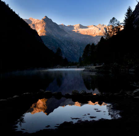 Reflection of mountain range in the lake in Val di Mello in a foggy morningの写真素材