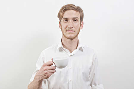 Young Adult Man in a White Shirt Holding a Cup of Coffee in His Handの写真素材