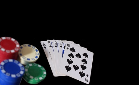 Playing cards showing royal flush with spades in a game of poker with chips to the side, set on black background.の写真素材