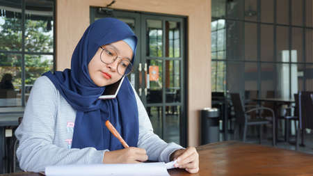 asian business girl is taking notes and is on the phoneの写真素材