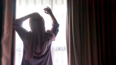 Asian girl is opening a window in the morningの写真素材