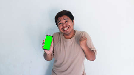 Asian fat man pointing to the cellphone with the green screenの写真素材