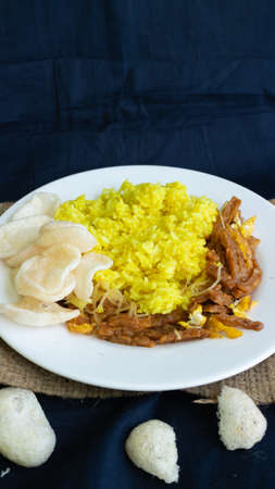 Nasi kuning or yellow rice, traditional food from Indonesia, for breakfast, combine wiith egg, tempeh, and crackers or kerupukの写真素材