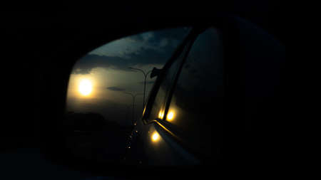Sunset from the car rearview mirror is on the highwayの写真素材