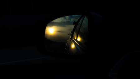 Sunset from the car rearview mirror is on the highwayの写真素材