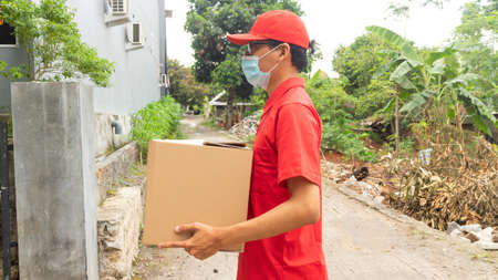 Asian young man delivery in red uniform with packagesの写真素材