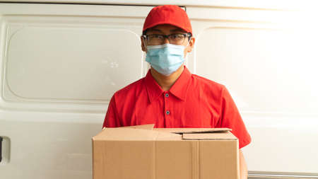 Asian young man delivery in red uniform with packagesの写真素材