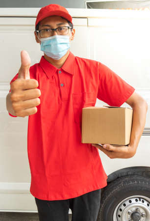 Asian young man delivery in red uniform with packages and OK expressionの写真素材