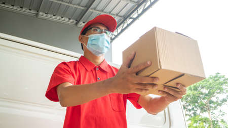 Asian young man delivery in red uniform with packagesの写真素材