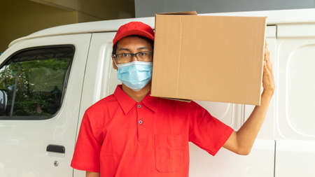 Asian young man delivery in red uniform with packagesの写真素材