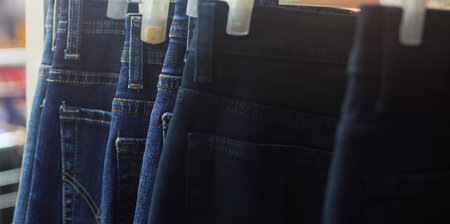 Closeup many jeans hanging on a rack. Row of pants denim jeans hanging in closet. concept of buy , sell , shopping and jeans fashionの写真素材