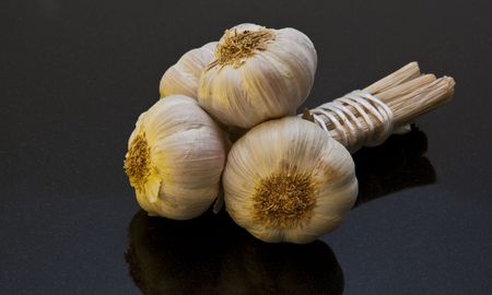 Three Bulbs of Garlic tied together on black marble work surface