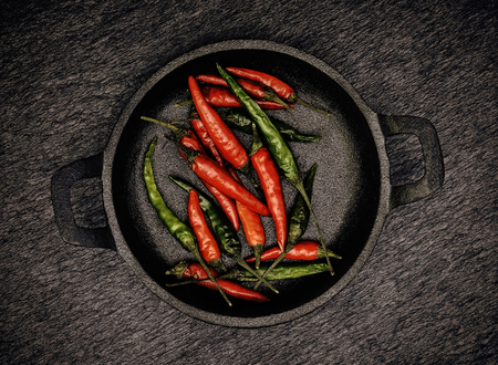 Red and Green Chillies in a black cast Iron bowl on a black rustic slate backgroundの写真素材