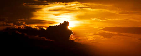 The sun partly covered by clouds in an orange sky の写真素材