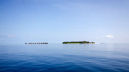 A small island in the Maldives with a number of cabins on stilts in the calm blue waterの写真素材