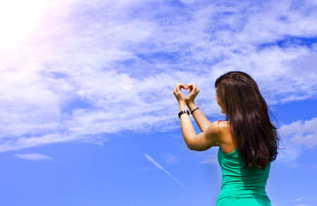 young women formed a heart with her hands in the skyの写真素材