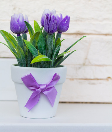 Decorative purple tulips in a white flower pot with a purple bow on the white stone background.の写真素材