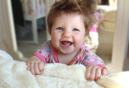 Little infant laughs, rejoices standing near the bed.の写真素材