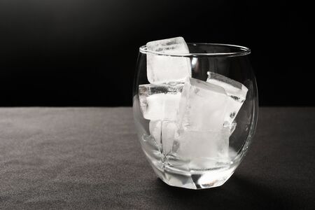 Ice cubes in glass on gray and black background.